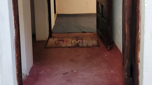 Ein Flur mit einer Holztür, einer blauen Matte am Eingang und einem kleinen Bild an der Wand.