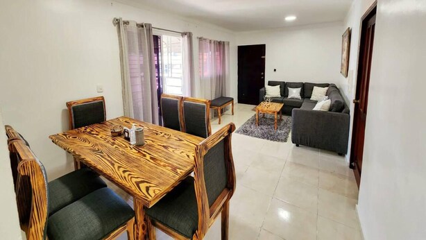 A living room with a sofa, a dining table with chairs, and a small coffee table. - Charming 3-bed Apartment 2 Bano Aire Acondicionado (Santo Domingo Oeste)