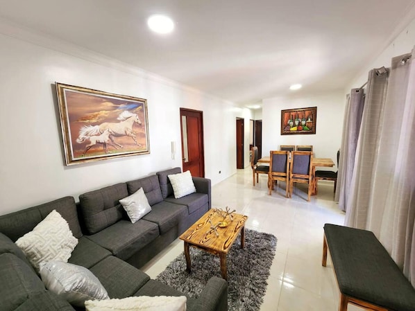 A living room with a sofa, a coffee table, a dining area with chairs and a table, and a painting on the wall.