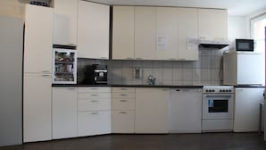 A kitchen with white cabinets, a built-in microwave, a coffee machine, and a dishwasher. - Stay2Night Hostel (Zürich)
