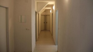 A narrow, well-lit hallway with a light-colored floor and walls, leading to a set of double doors at the end. - Stay2Night Hostel (Zürich)
