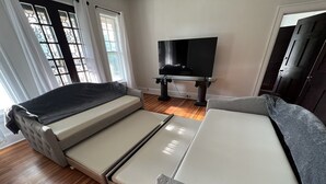 Een kamer met een slaapbank, een flatscreen-tv en een raam met decoratieve glaspanelen.