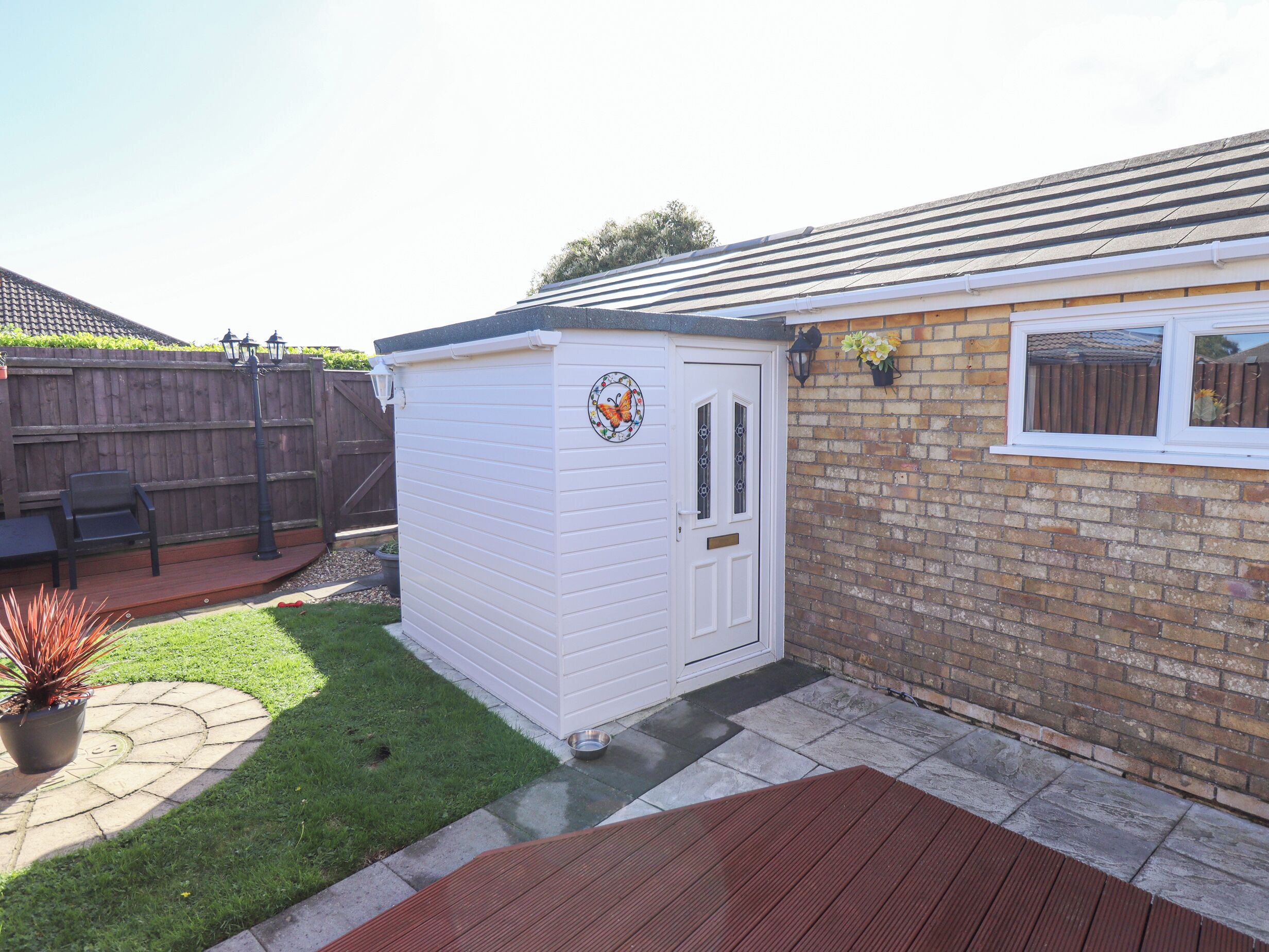 A small white shed with a butterfly design, a brick wall, and a window.