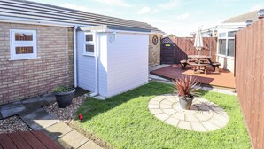 A backyard with a patio, a wooden fence, a shed, and a brick wall. - Lockdown Lodge (Mablethorpe)