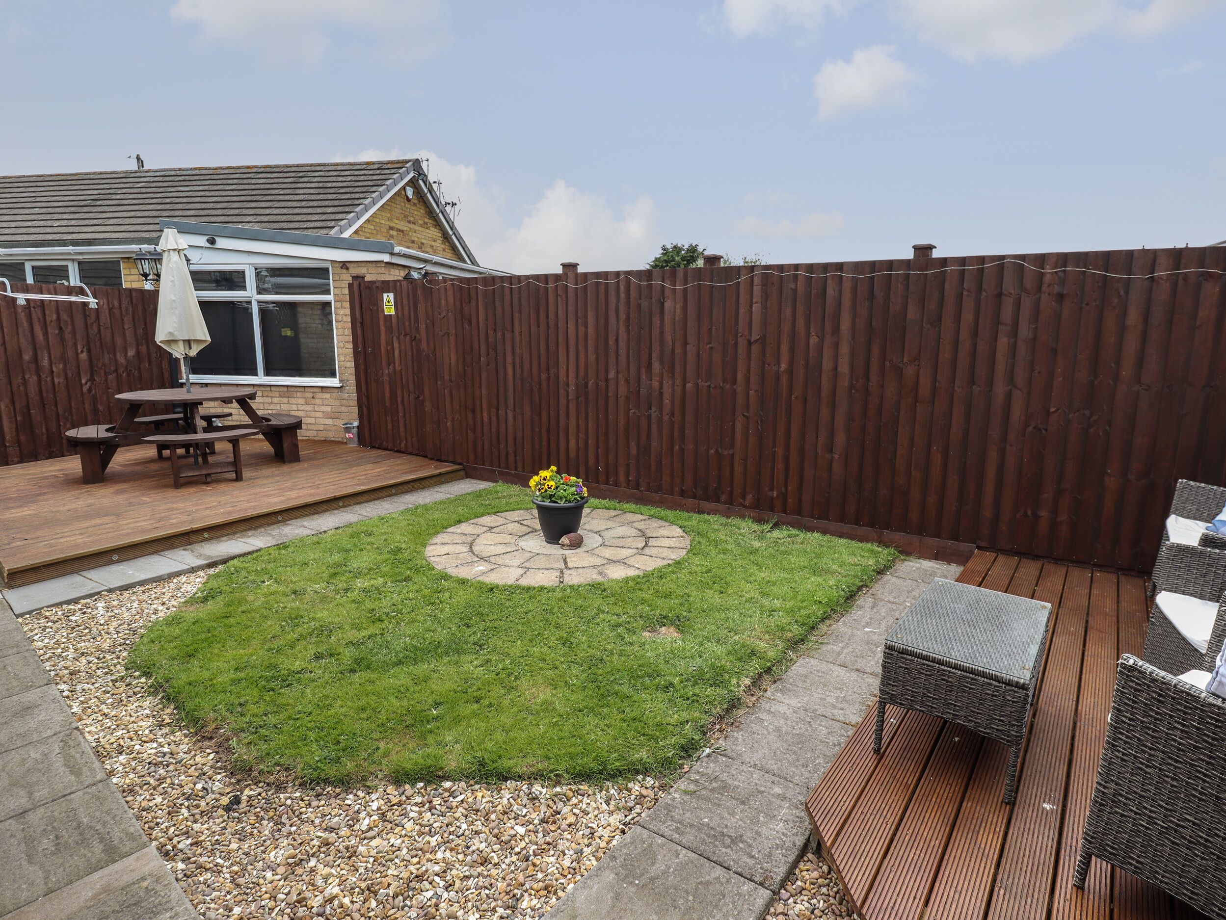 A backyard with a wooden deck, a picnic table, a small garden with flowers, and a fenced area.