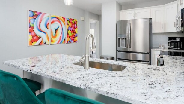 A modern kitchen with a marble countertop, stainless steel appliances, and teal chairs. - Candy Land- Downtown ILM (Wilmington)