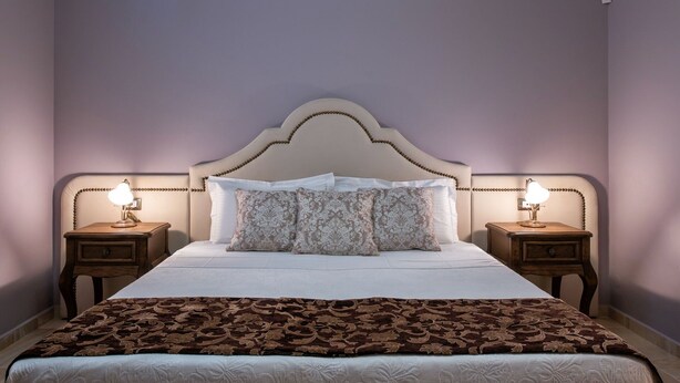 Un lit bien fait, avec une tête de lit à motifs, deux tables de chevet avec des lampes et un plaid marron à motifs.