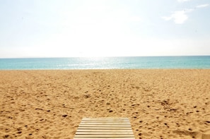 Ein sandiger Strand mit einer hölzernen Promenade, die zum Wasser führt.