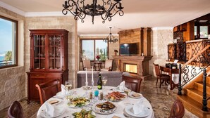 Un coin repas avec une table ronde dressée pour le repas, une cheminée et une vue sur l’extérieur.