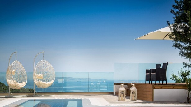 A rooftop infinity pool with hanging egg chairs and a view of the ocean.