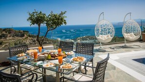 A dining table with food and drinks, two hanging chairs, and a view of the sea.