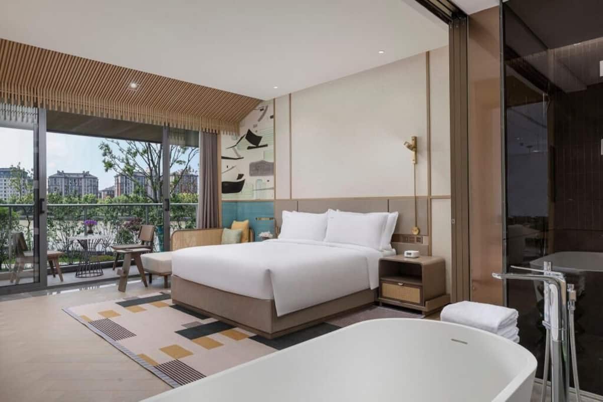 Un dormitorio moderno con una cama grande, una bañera y un balcón con vistas a edificios.