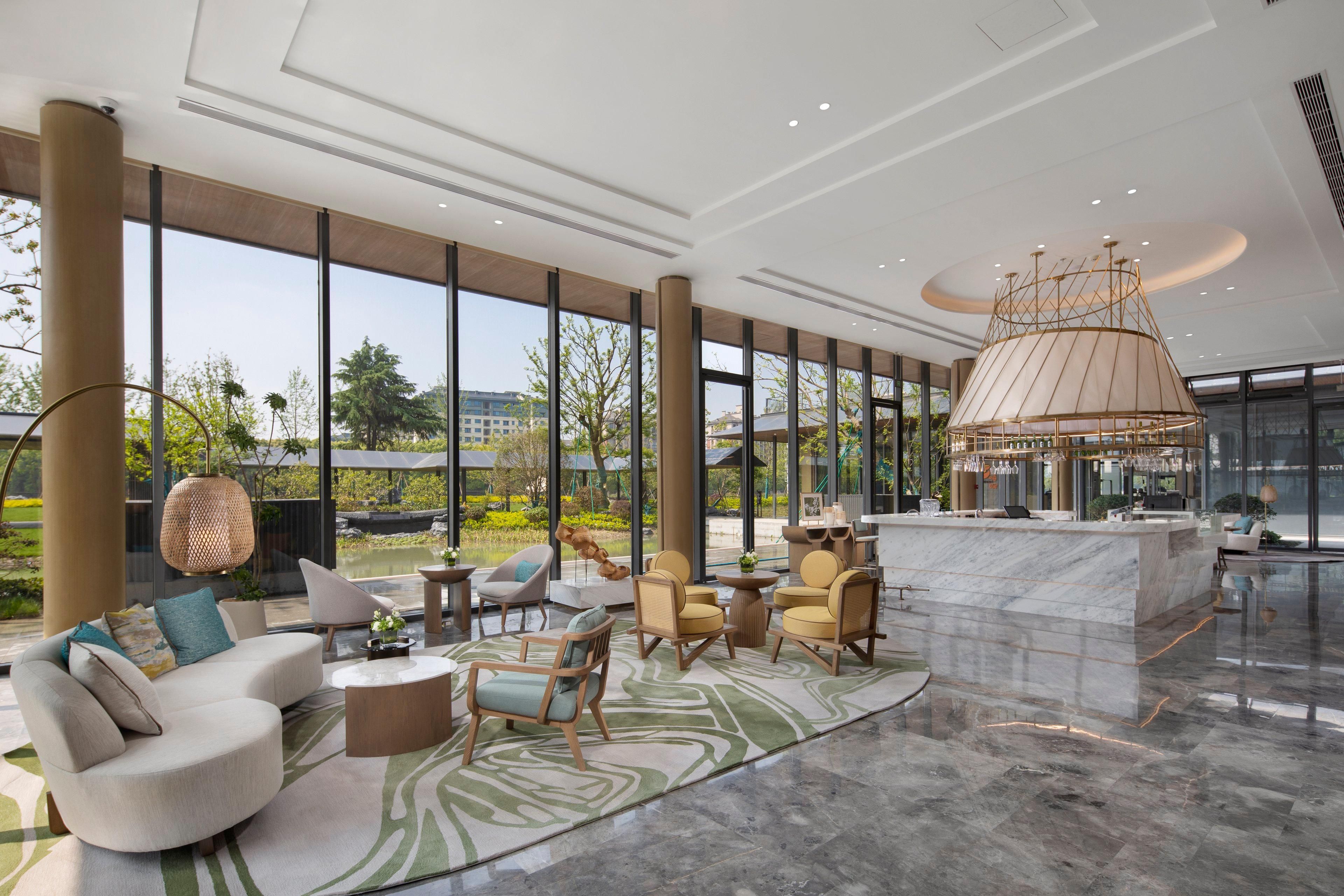 A spacious lobby with a large seating area, a central bar, and large windows offering a view of the outdoors.