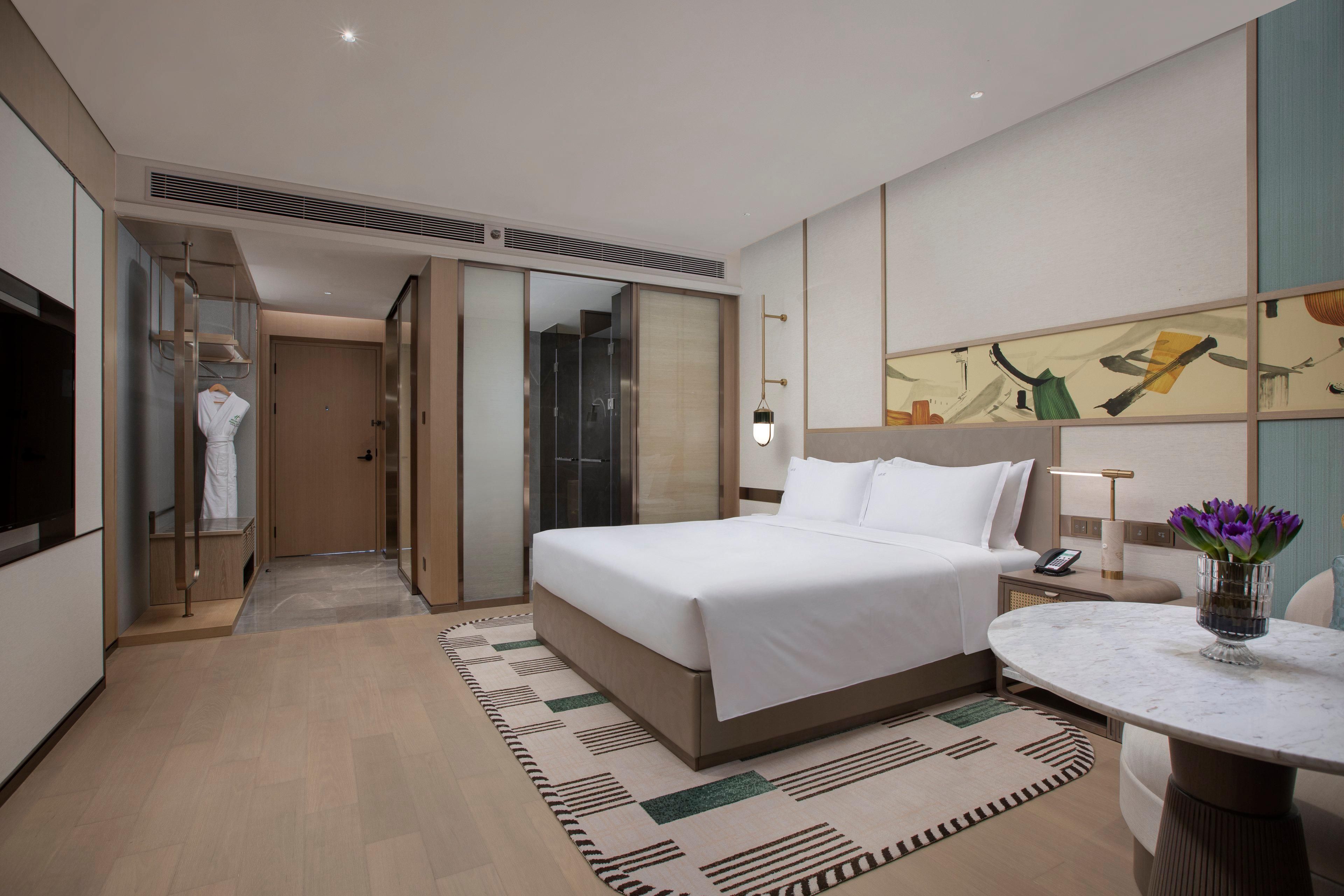 Een hotelkamer met een bed, nachtkastje, lamp en een schilderij aan de muur.