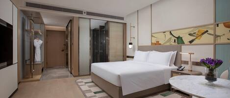 A hotel room with a bed, bedside table, lamp, and a painting on the wall.