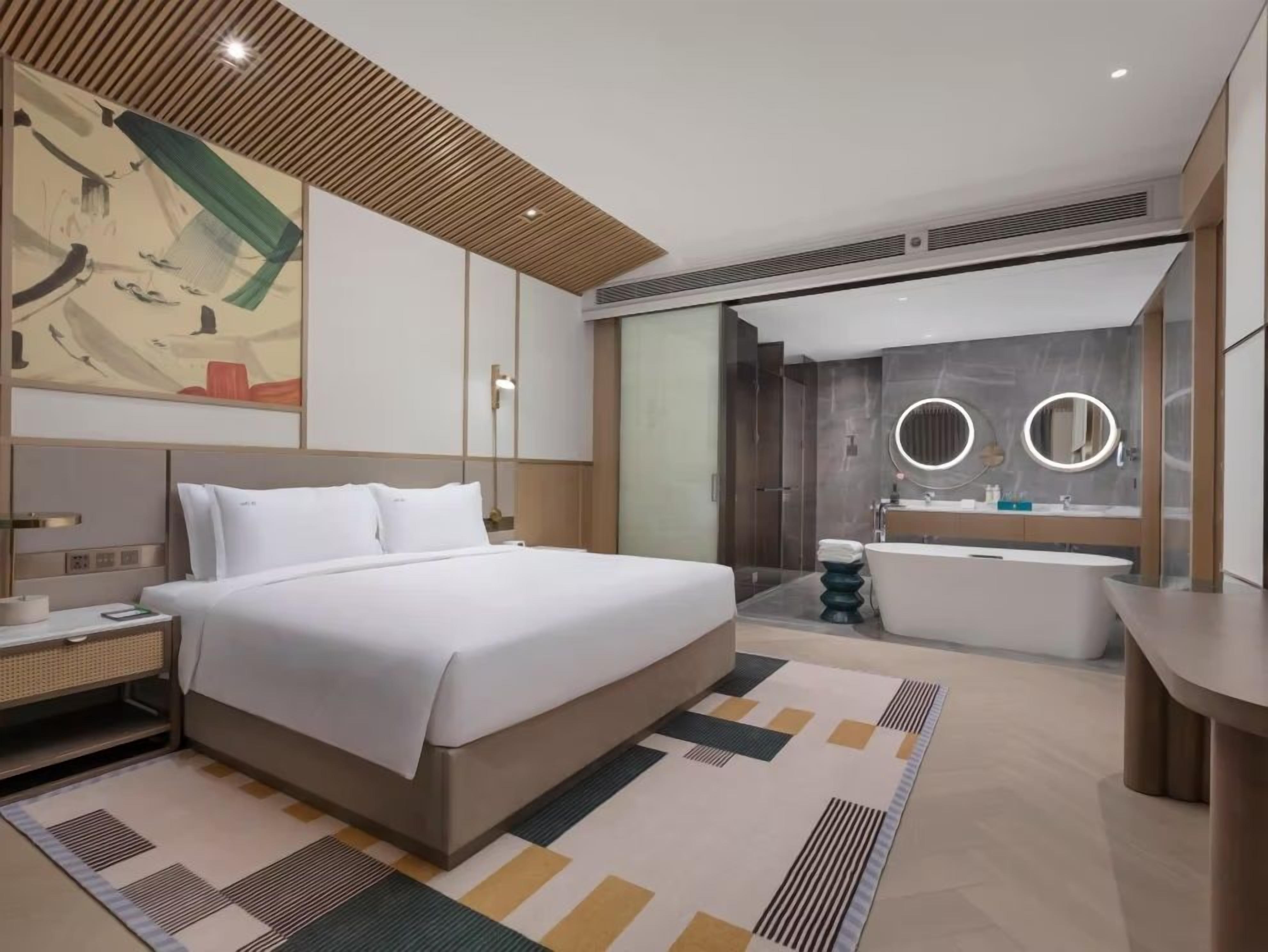 Una habitación de hotel moderna con una cama grande, un baño independiente con bañera y un espejo amplio.