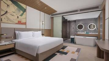 Una habitación de hotel moderna con una cama grande, un baño independiente con bañera y un espejo amplio.