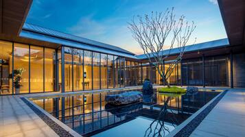 A modern building with a glass facade, a reflective water feature, and a tree in the courtyard.