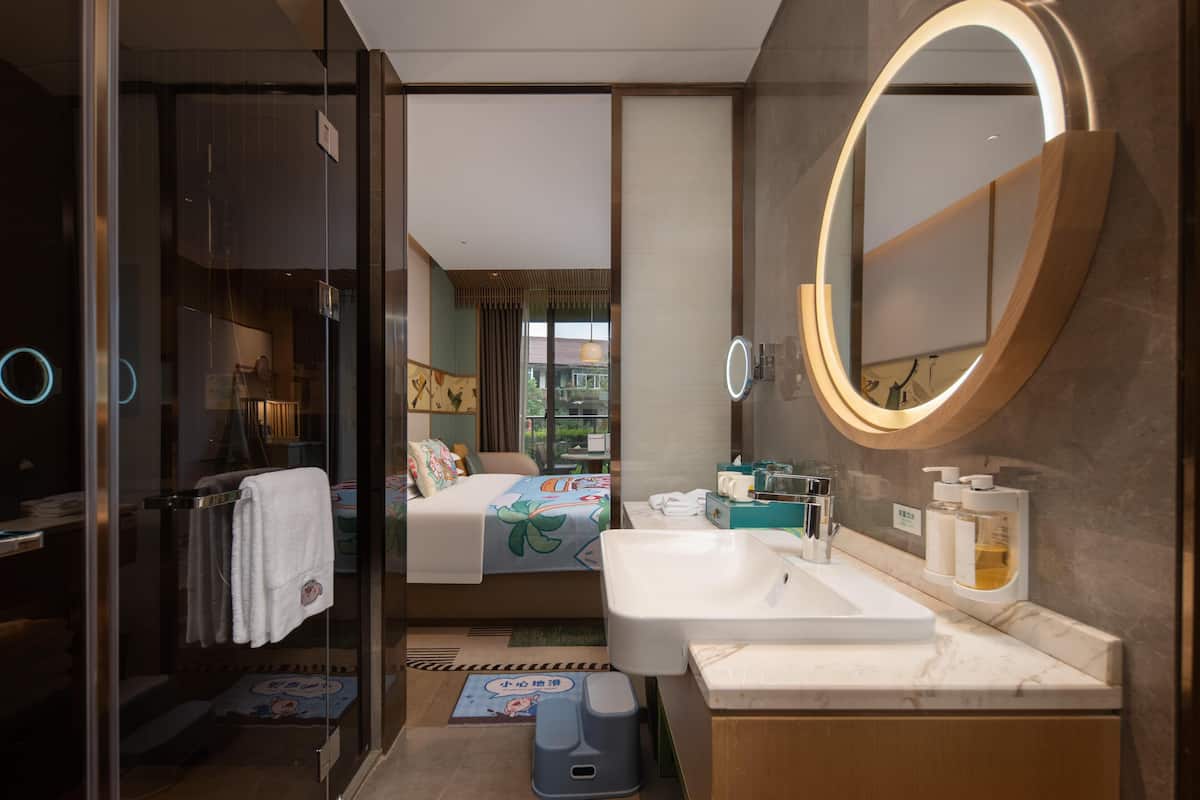 Un baño de hotel moderno con un espejo grande, un lavamanos y una zona de ducha.