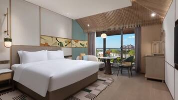 A modern hotel room with a large bed, a dining area, and a view of the city.