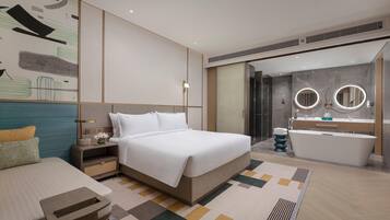 A modern hotel room with a large bed, bedside table, and a bathroom with a bathtub and two round mirrors.