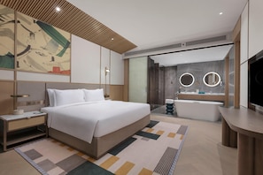 Une chambre d’hôtel moderne avec un grand lit, une table de chevet, une commode, une salle de bain avec baignoire et un grand miroir.