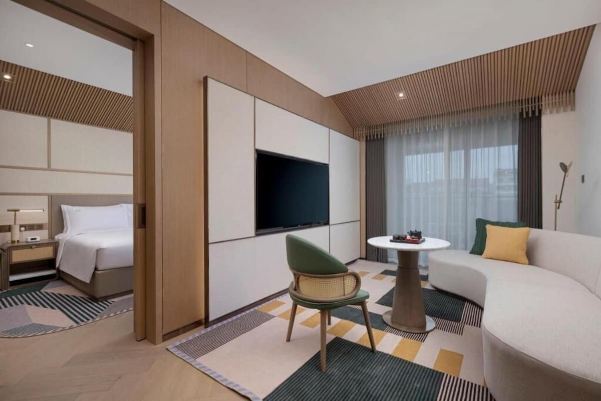 Una habitación de hotel con cama, televisión, sofá, sillón y una pequeña mesa.
