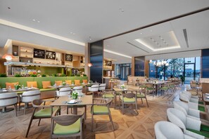 Un restaurant moderne offrant différents types de sièges, notamment des banquettes et des tables, et dont la cuisine est visible.