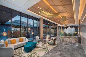 Eine geräumige Lobby mit Rezeption, Sitzgelegenheiten und großen Fenstern mit Blick ins Freie.
