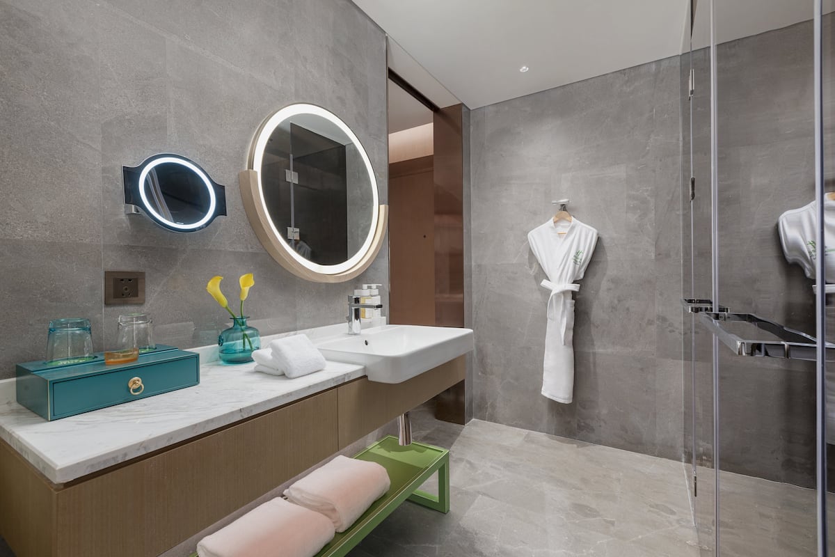 Un baño moderno con tocador de mármol, un espejo grande, una bata colgada en la pared y una cabina de ducha de vidrio.