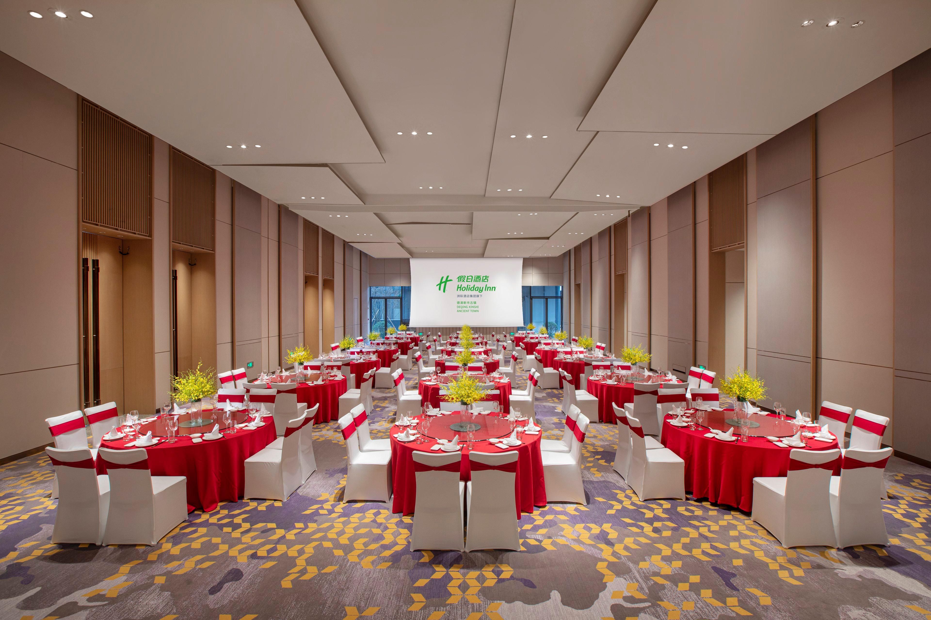 A conference room with round tables, red tablecloths, white chairs, and a projection screen at the front.