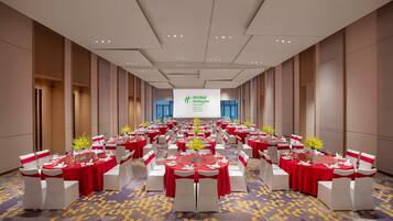 A conference room with round tables, red tablecloths, white chairs, and a projection screen at the front.