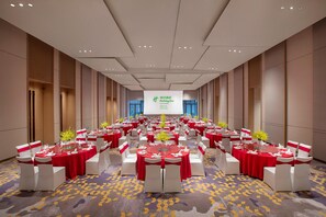 A conference room with round tables, red tablecloths, white chairs, and a projection screen at the front. - Holiday Inn Deqing Xinshi Ancient Town (Huzhou)
