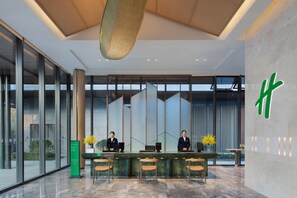 A modern hotel reception area with a reception desk, two staff members, and a large glass wall. - Holiday Inn Deqing Xinshi Ancient Town (Huzhou)