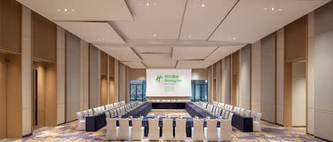 A conference room with a long table and chairs, a large screen displaying text, and a patterned carpet.