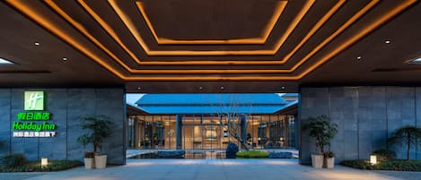 A modern hotel entrance with a geometric ceiling design and a large glass facade.