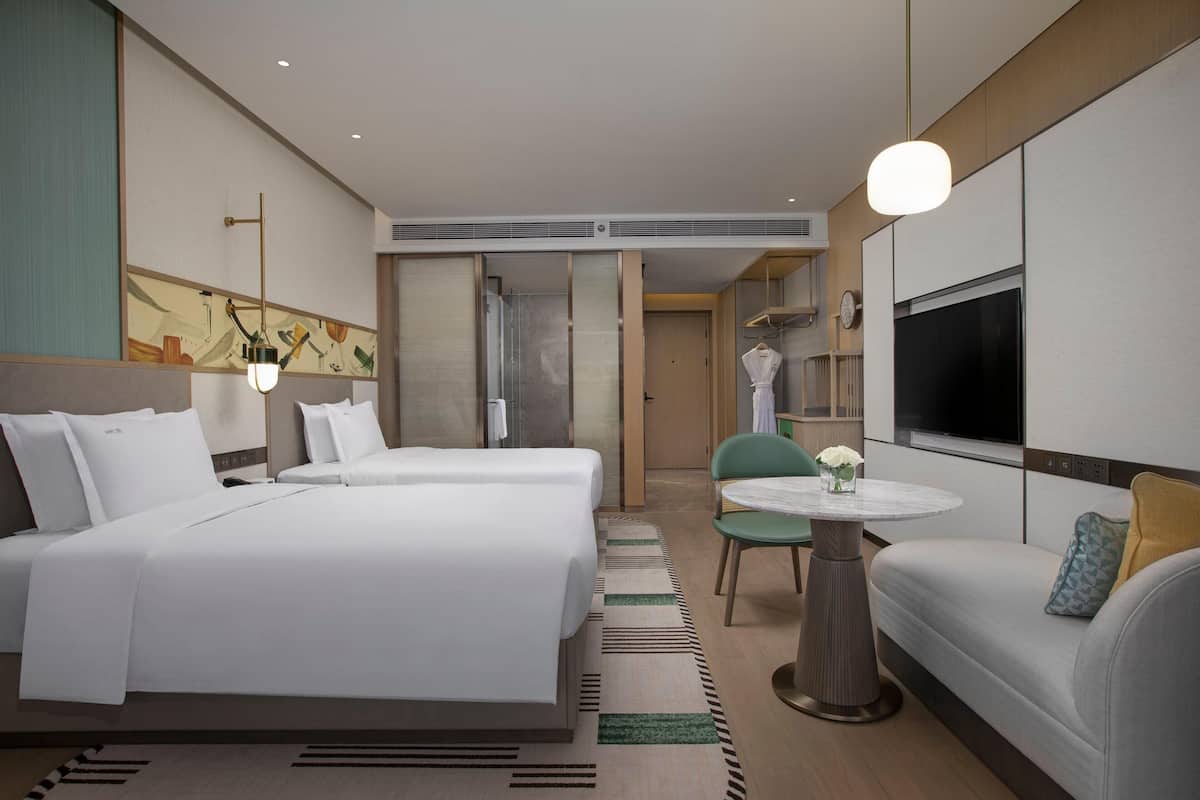 Una habitación de hotel con dos camas, un sofá, una mesa redonda y un televisor.