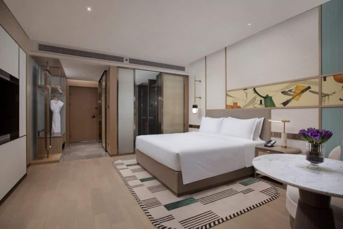 Una habitación de hotel con cama, mesita de noche, lámpara y un cuadro en la pared.