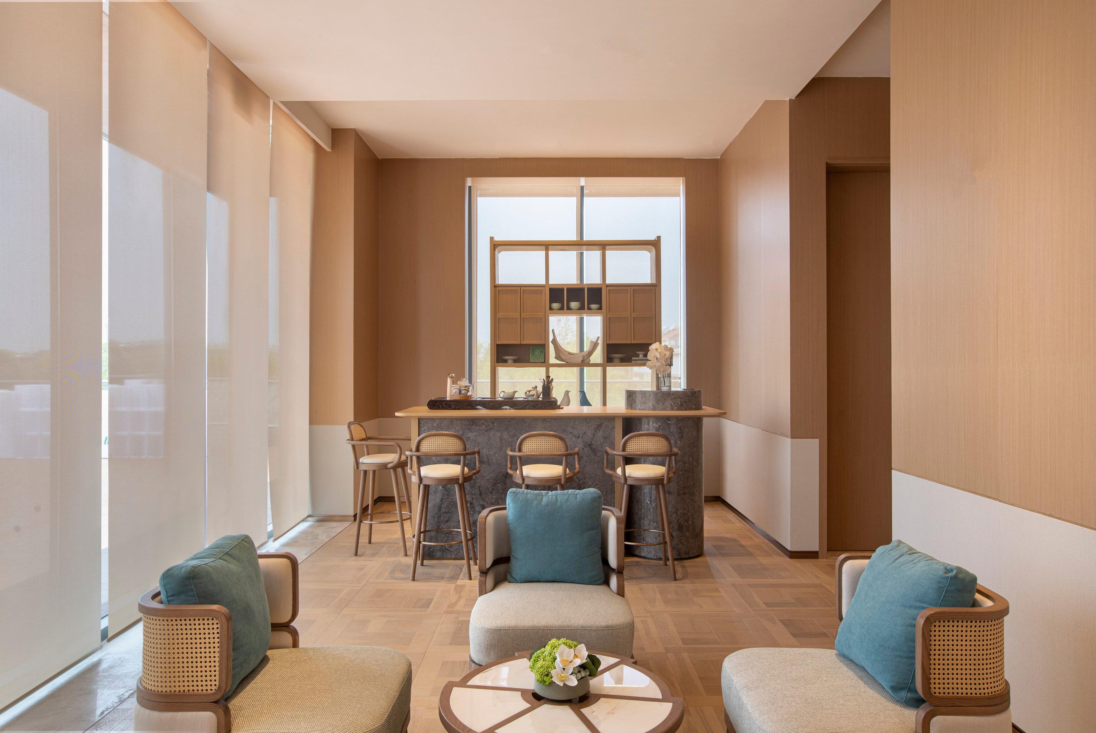 A modern hotel lobby with a bar area, seating with cushions, and a large window providing natural light.