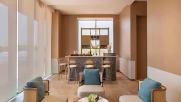 A modern hotel lobby with a bar area, seating with cushions, and a large window providing natural light.