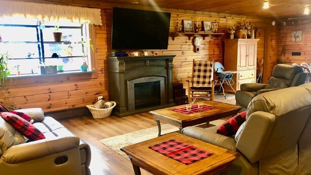 A cozy log cabin interior with a fireplace, leather sofas, a television, and wooden floors. - Lazy Bear Cabin Pet Friendly-Handicap Accessible (Frewsburg)
