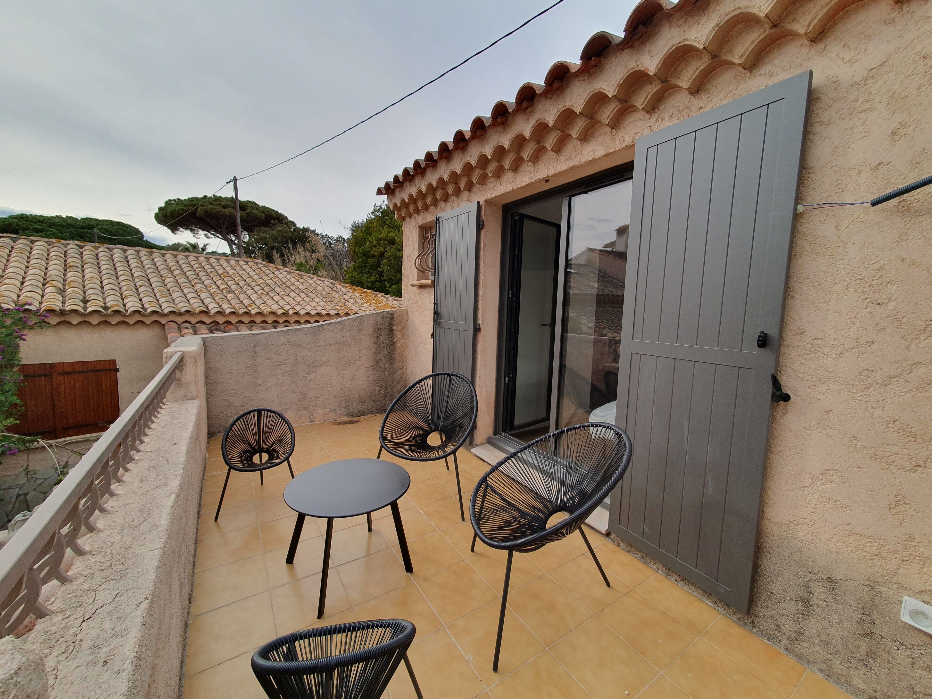 A small patio with a table and four chairs, a sliding glass door, and a tiled roof.