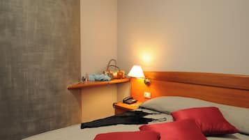 Une chambre d’hôtel comprenant un lit, une table de chevet, une lampe et une étagère où sont posés des objets personnels.