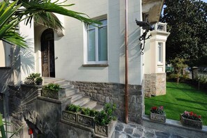 Ein Haus mit einer Steinstufe, die zu einer Tür führt, ein kleiner Garten mit Kübelpflanzen und ein Metallpfosten mit verziertem Knauf.