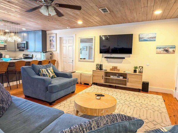 A living room with a sofa, a coffee table, a TV, and a kitchen in the background.