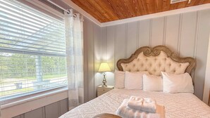 A bedroom with a bed, a nightstand, a lamp, and a window with blinds. - Pet Friendly Sleeps 9 Golf Cart Hot Tub - Weekly Discounts (St.Geroge Island)