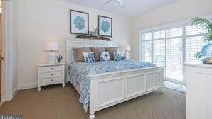 A bedroom with a large bed, two nightstands, a ceiling fan, and a window with blinds. - Luxury 3BR, 4BA Oasis: Beach is 2 blocks away, Indoor Pool, sleeps 8! Waterfront (Ocean City)