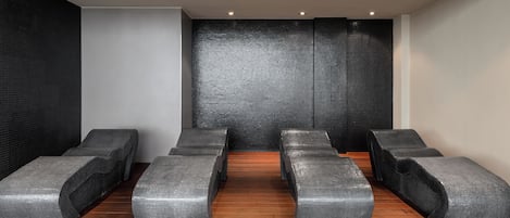 A spa room with six black cushioned benches arranged in two rows.