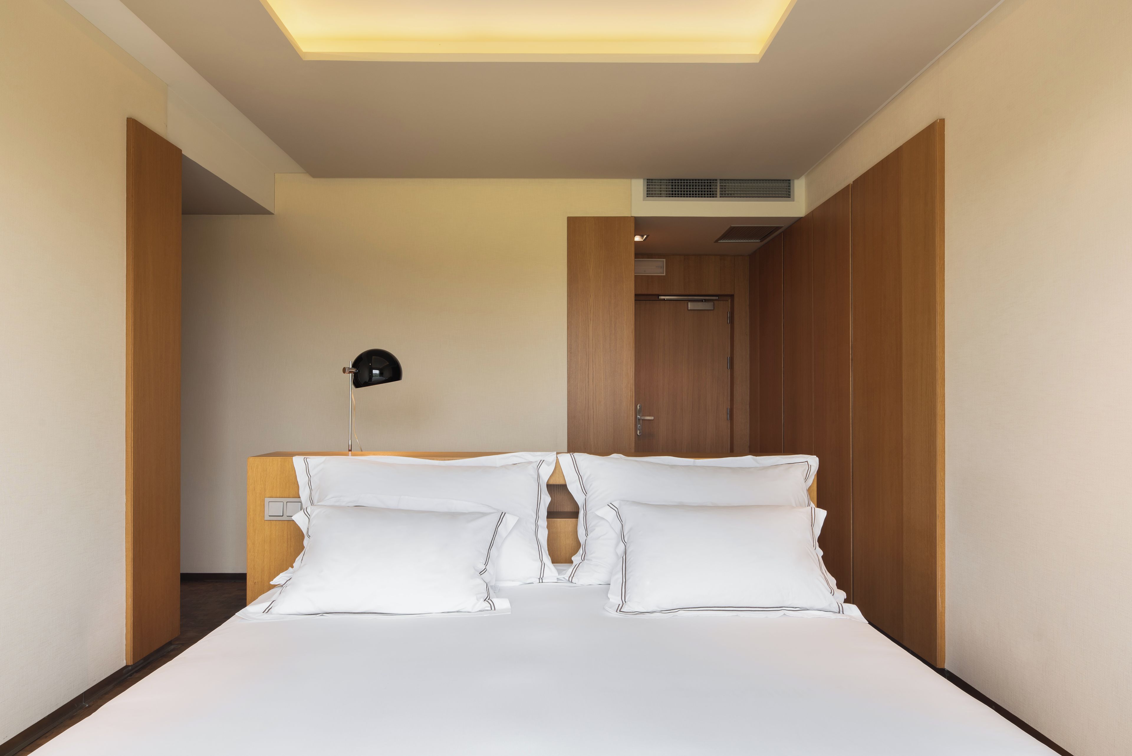 Una habitación de hotel moderna con una cama bien hecha, una lámpara de noche y un armario de madera.