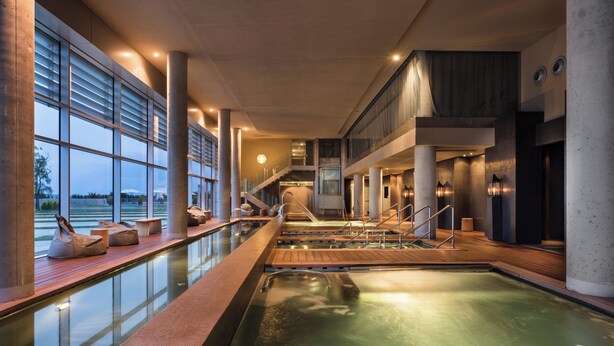 A modern indoor pool area with a clear view of the outdoors, a wooden deck, and a staircase leading to an upper level. - Valbusenda Hotel Bodega and Spa (Toro)